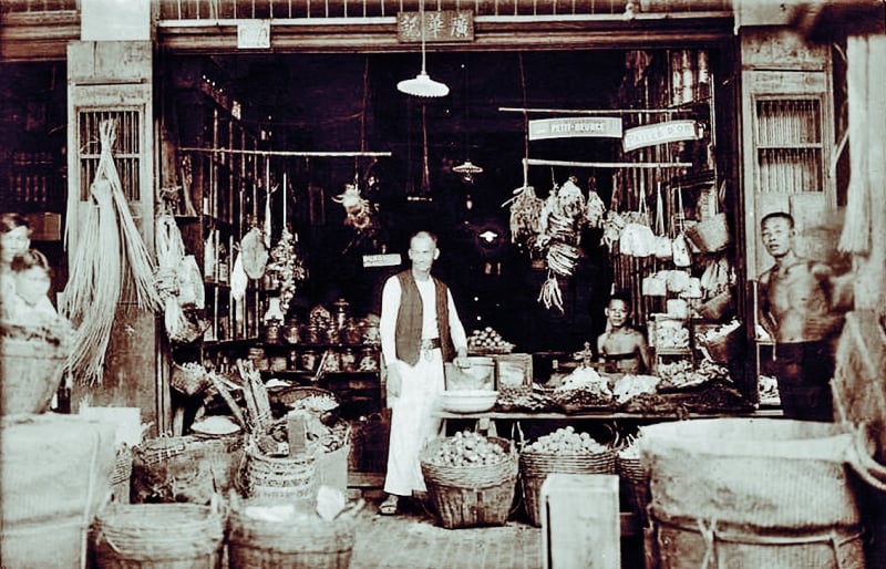 A 1931 photo of a Chinese grocer amidst his merchandise on display. Chinese from Canton built streets with rows of shophouses in Cholon: shops built in between houses on either side and with residential accommodation on the upper floors.
